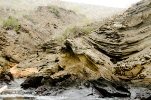 The island is made of layer upon layer of ash and silt, metamorphosed by pressure and time into rock.  The weight of the ask and silt droops unenvely over time, based on the weight of the layers above and so forms these liquid looking ripples and rents, which later are converted to stone.